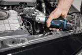 A person uses a cordless ratchet wrench to tighten a bolt in a car engine.