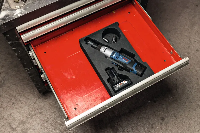 Cordless ratchet wrench set with battery and socket stored in a red toolbox drawer.