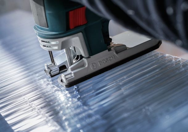 Jigsaw cutting clear acrylic sheet along straight lines.