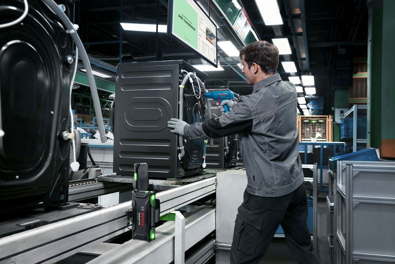 A person wearing safety equipment assembles an appliance on a factory production line with a smart controller.