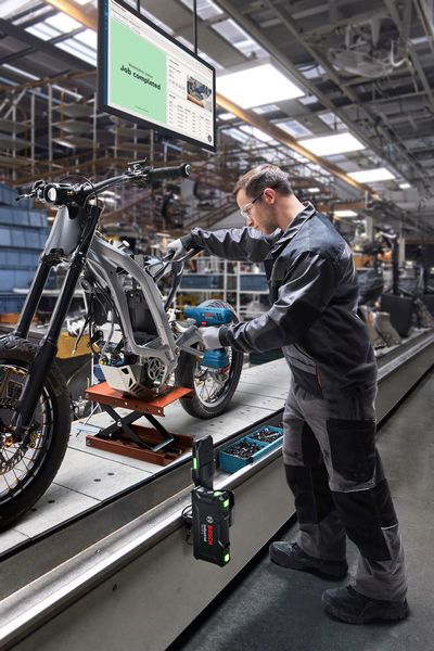 A person wearing safety equipment assembles a motorcycle frame at a factory workstation.
