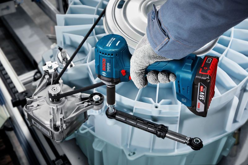 A person wearing safety equipment uses a cordless impact wrench on industrial machinery.