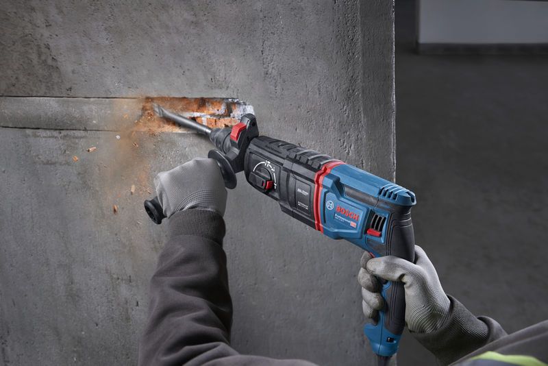A person wearing safety equipment uses a rotary hammer to chisel a groove in concrete.
