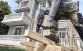 A person wearing safety equipment drills into stacked wooden beams at a construction site.