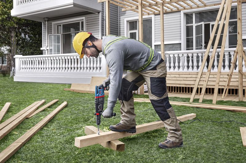 A person wearing safety equipment drills into wooden beams at a construction site.