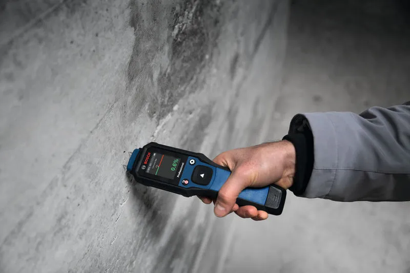A person measures wall moisture using a material moisture meter.