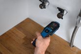 A person uses a material moisture meter to check moisture in a wooden countertop.