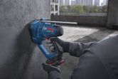 A person wearing safety equipment cuts a threaded rod against a concrete wall.