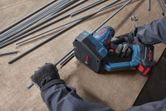 A person wearing safety equipment cuts a threaded rod using a cordless rod cutter.
