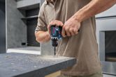 A person drills a hole into a countertop with a cordless power tool.