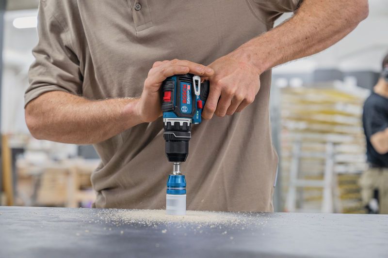 Person operating a cordless drill with a hole saw bit to cut into a work surface.