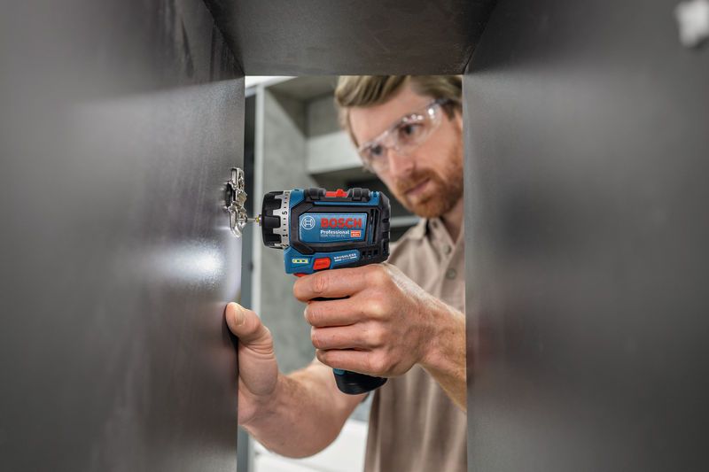 A person wearing safety equipment uses a screwdriver to install a cabinet hinge.