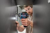 A person wearing safety equipment uses a screwdriver to install a cabinet hinge.