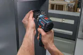 Person uses a cordless screwdriver to drive a screw into a metal panel.