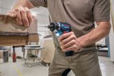 A person drives a screw into stacked wood using a cordless screwdriver.
