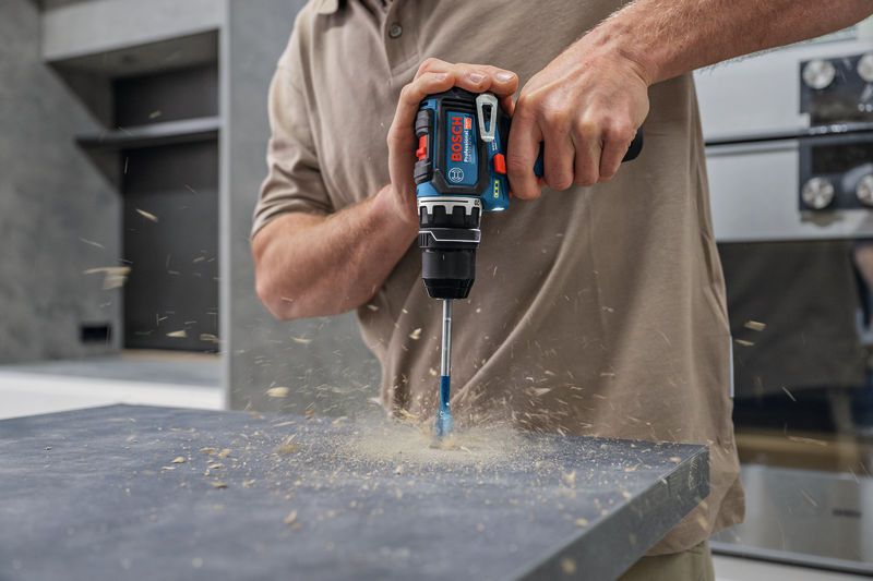 A person drills into a countertop, wood shavings scattering.