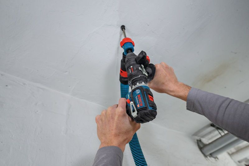 A person uses a cordless screwdriver with a dust extraction attachment on a ceiling.