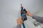 A person uses a cordless screwdriver with a dust extraction attachment on a ceiling.