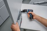 A person uses a screwdriver to fasten a drawer slide onto a cabinet panel.