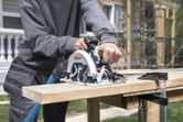 A person cuts a wooden board with a cordless circular saw at a construction site.