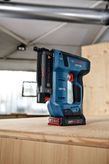 Cordless electric nail gun resting on a wooden surface in a workshop.