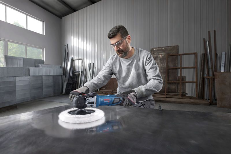A person wearing safety equipment uses a polisher on a large metal surface.
