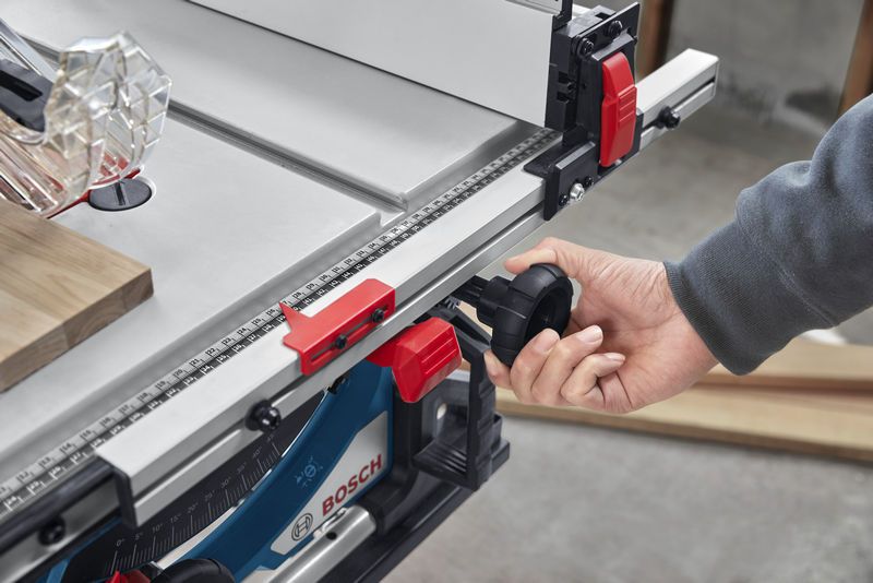 Person adjusts table saw fence using a black knob in a workshop.