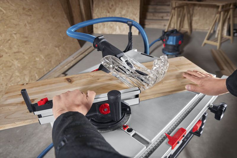 A person pushes wood through a table saw in a workshop.