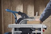 A person guides wood through a table saw with dust extraction in a workshop.