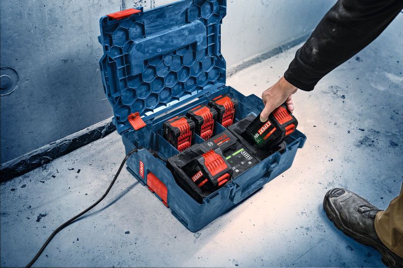 A person places a battery into a portable charger station on a workshop floor.