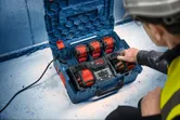 A person wearing safety equipment operates a multi-battery charging station on a job site.