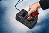 A person inserts a cordless tool battery into a charging station on a concrete floor.