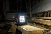 Cordless jobsite light illuminating wooden planks in heavy rain at a construction site.