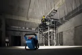 Cordless jobsite light illuminating a person wearing safety equipment on scaffolding.