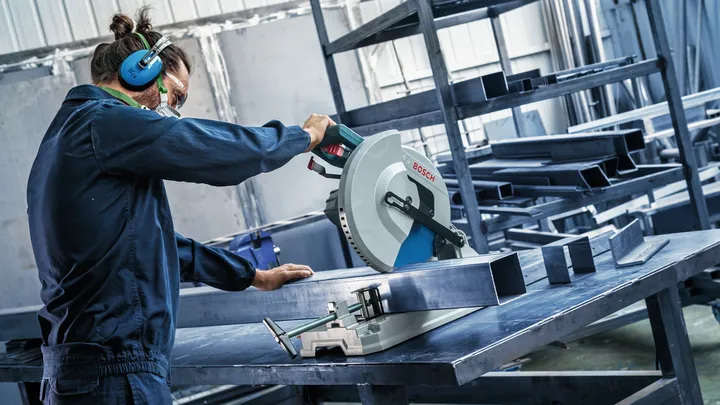 Object #200585209: 7557706_app_web_03 Person wearing safety equipment uses a circular saw to cut a metal beam on a worktable.