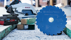 Circular saw blade stands upright on a workbench beside a cordless battery and saw.
