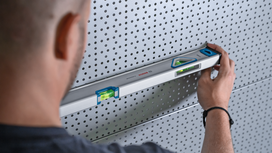 Person aligns a spirit level against a perforated metal panel.