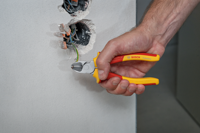 Person cuts a green electrical wire coming from a wall socket using insulated pliers.