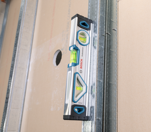 Spirit level measuring alignment on a drywall panel.