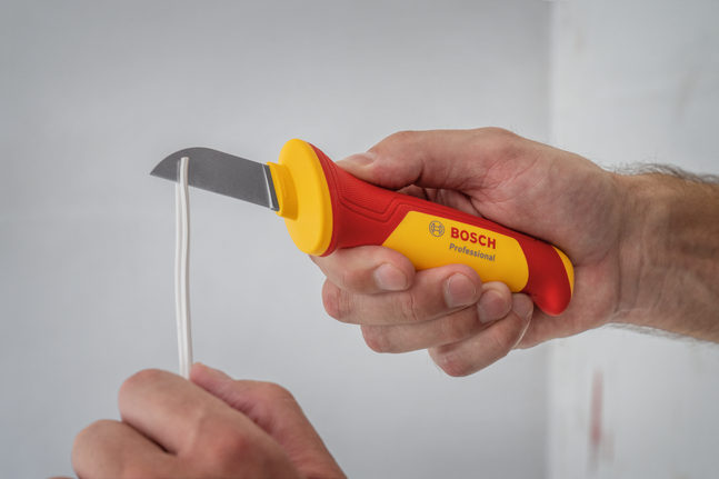 Person uses a curved utility knife to strip insulation from an electrical wire.