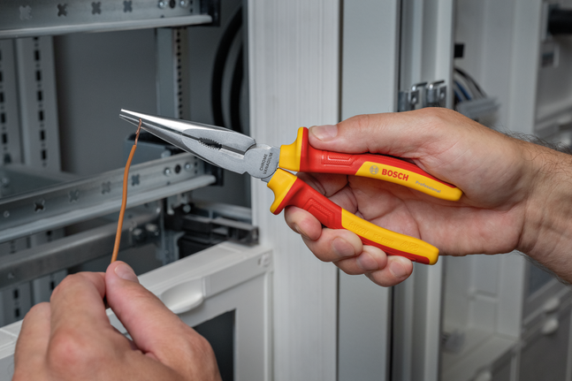 Person uses insulated pliers to bend wire near an electrical panel.
