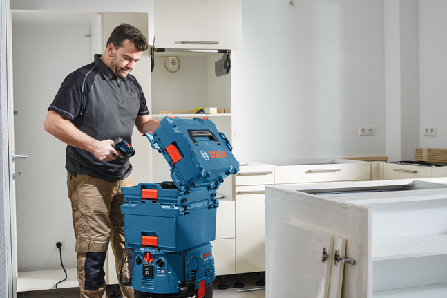 A person in work clothes opens a tool storage case in a kitchen under renovation.
