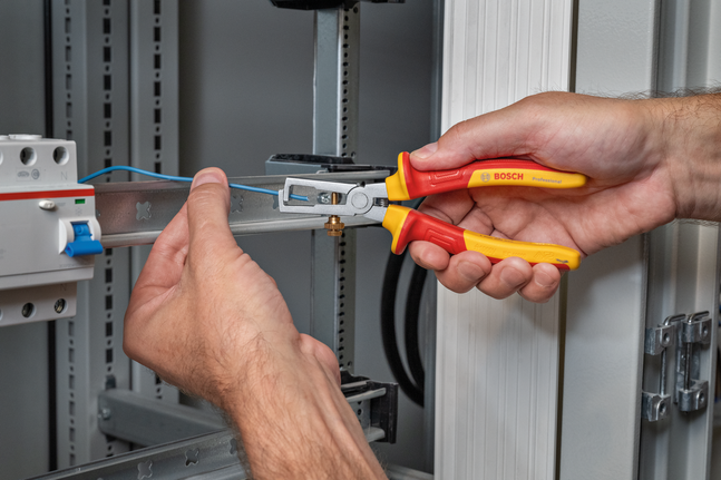 Person uses insulated pliers to strip a blue wire in an electrical panel.