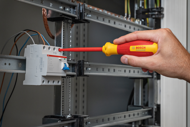 Person uses insulated screwdriver to adjust wiring in an electrical panel.