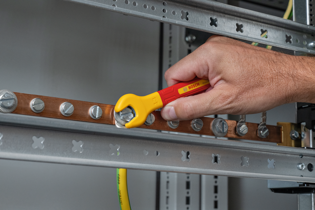 Person tightens a bolt on a copper busbar using an insulated wrench.