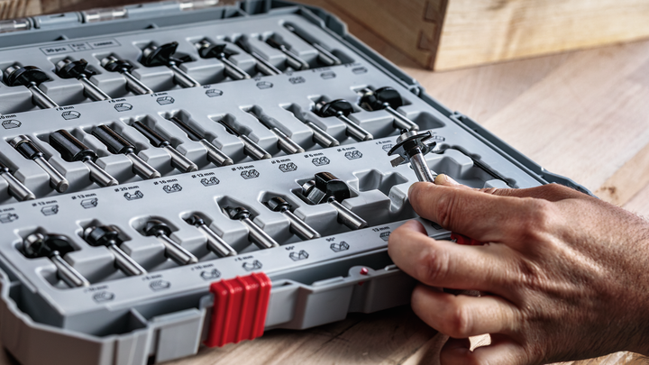 Object #200587566: 7437800_app_web_01 Person selecting a router bit from an organized tool case on a wooden surface.