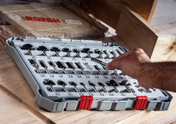 Person selects a router bit from an organized drill bit set on a wooden workbench.