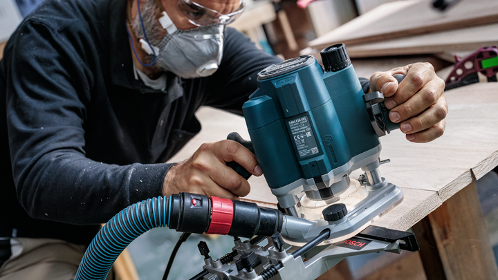 Object #200587643: 7437772_app_web_05 Person wearing safety equipment uses a power router to shape the edge of a wooden board.