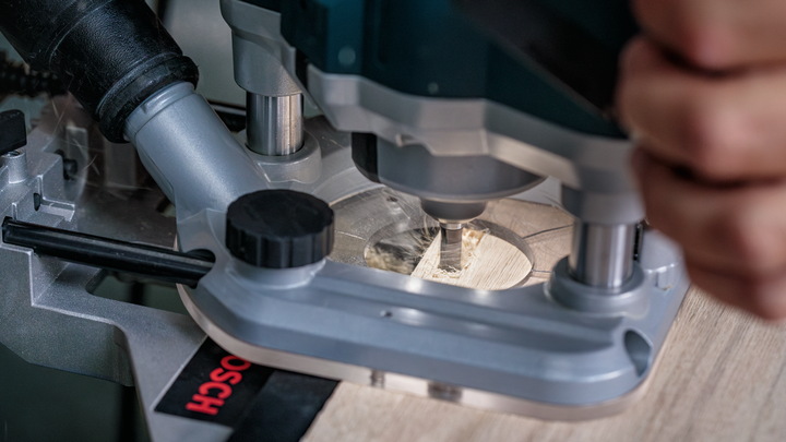 Person guides a woodworking router along a plank, creating precise grooves.