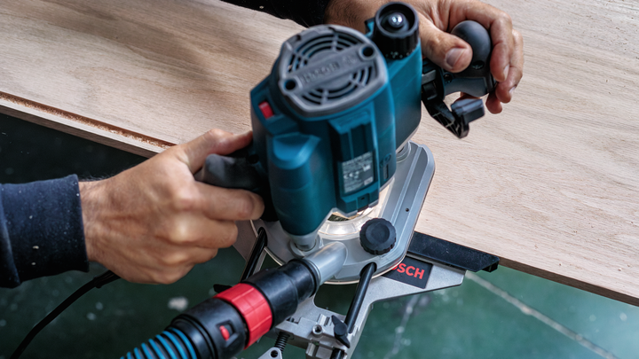 Person guiding a power router along the edge of a wooden board.